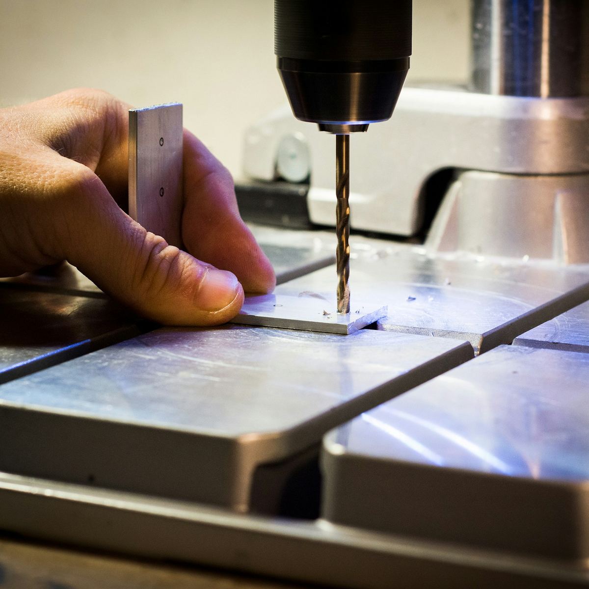Een hand houdt een aluminium plaatje onder een kolomboor